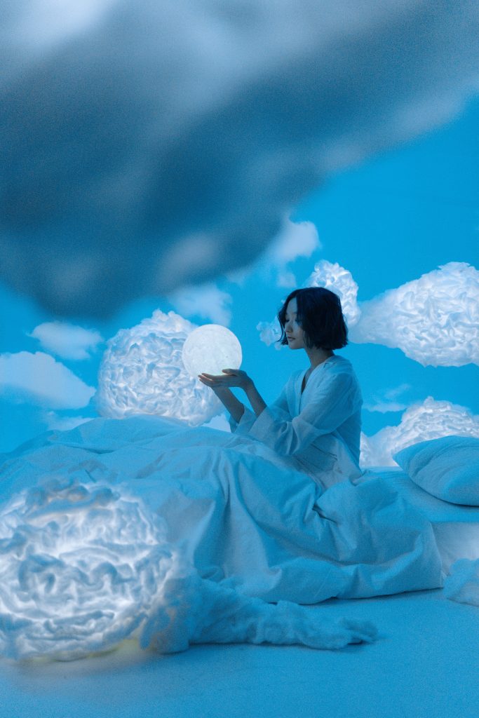 Frau mit schwarzem Haar in Bett zwischen Wolken