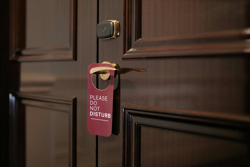 eine geschlossene Hotelzimmertür aus dunklem Holz, an der ein "Do not disturb"-Schild hängt