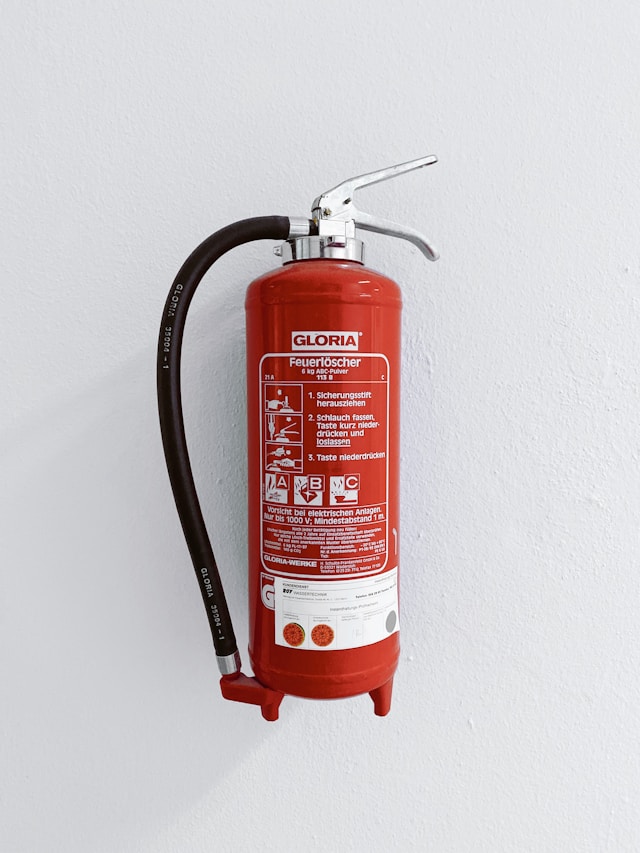 roter Feuerlöscher mit deutscher Anleitung vor weißer Wand