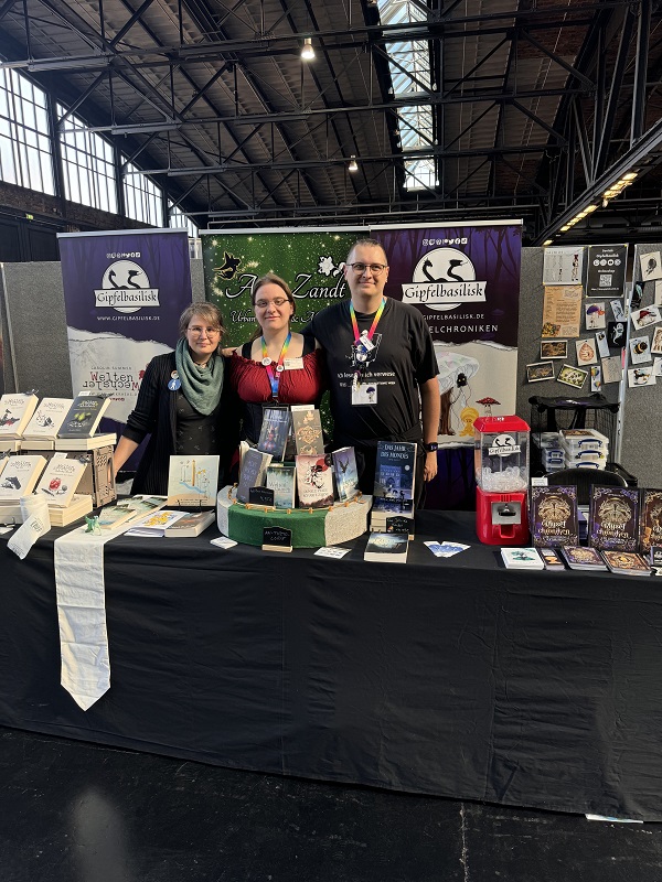 Foto der drei Autor*innen Carolin Summer, Anne Zandt und Gipfelbasilisk an ihrem gemeinsamen Messestand auf der Buch Berlin 2024