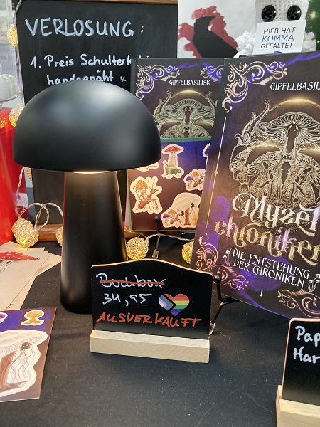 Foto eines Messestandes des Autors Gipfelbasilisk, das ein Preisschild mit durchgestrichenem Preis und dem Wort "Ausverkauft" darunter zeigt