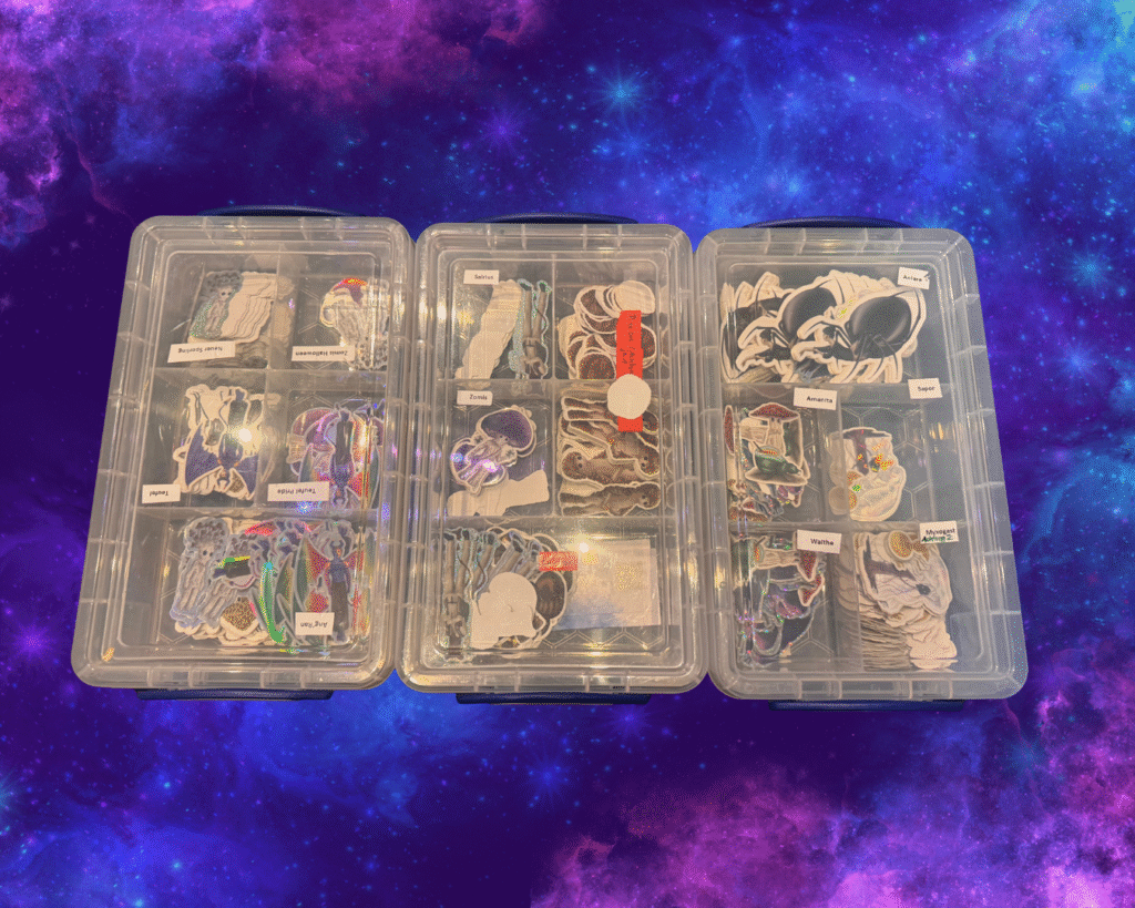 Foto mehrerer Sortierboxen, in denen verschiedene Sticker liegen, vor einem lila Galaxyhintergrund