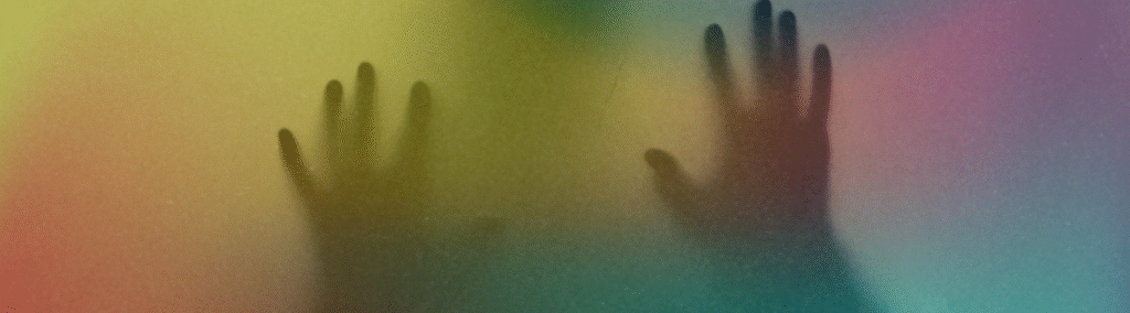 Silhouetten zweier Hände, die sich wie zum Ausbruch gegen ein Glas drücken, alles ist in matten Regenbogenfarben getaucht